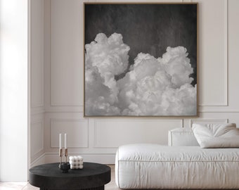 May include: A black and white photograph of fluffy clouds against a dark sky. The image is framed and hanging on a white wall above a white couch.