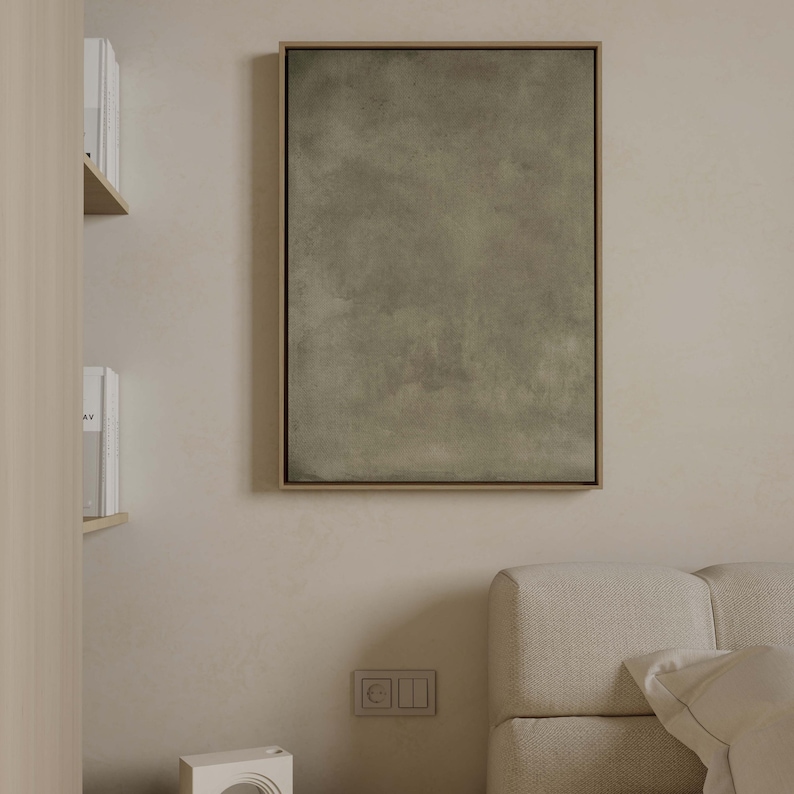 May include: A framed abstract art piece with a muted green and gray color palette. The artwork is rectangular and hangs on a beige wall. The frame is a light brown color. The image is in a bedroom setting.