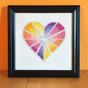 May include: A framed cross-stitch design of a colorful heart with a geometric pattern. The heart is made up of shades of yellow, orange, pink, and purple.