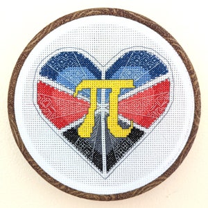May include: A white cross-stitch embroidery hoop with a colorful heart design. The heart is made up of red, blue, and black geometric shapes. The letter "π" is in the center of the heart and is yellow.