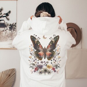 May include: White hoodie with a large butterfly design on the back. The butterfly is surrounded by flowers and has a crescent moon above it.