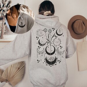 May include: A gray hooded sweatshirt with a black and white design of moons, flowers, and stars on the back.