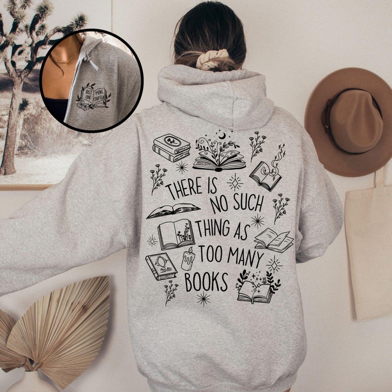 A gray hooded sweatshirt with a black graphic print of books, stars, and flowers. The text on the graphic reads 'There is no such thing as too many books'.