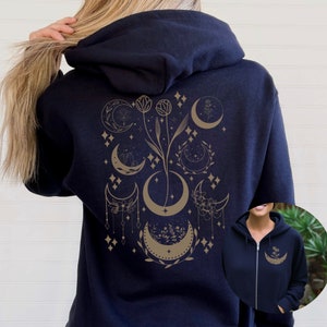 May include: A navy blue zippered hoodie with a gold floral and crescent moon design on the back. The design features multiple moons, stars, and flowers.