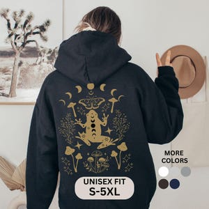 May include: A black unisex hoodie with a gold graphic of a frog, mushrooms, and moon phases. The text "UNISEX FIT S-5XL" is displayed on the bottom. Additional color options are shown on the right.