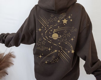 Peut inclure: Un sweat à capuche marron avec un imprimé doré d'étoiles, de planètes et d'étoiles filantes au dos.