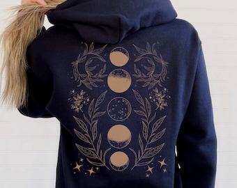 May include: Navy blue hoodie featuring a celestial design on the back. The design includes phases of the moon, leaves, stars, and floral elements in a light brown color. The hoodie has a hood and long sleeves.