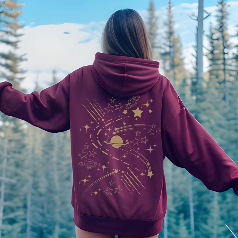 May include: Burgundy hoodie with a gold design of stars, planets, and shooting stars on the back.