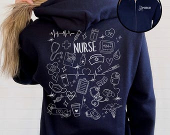 May include: Navy blue zip-up hoodie with a white graphic design on the back featuring medical symbols, a stethoscope, and the word "NURSE". The hoodie also has a small embroidered name on the chest.