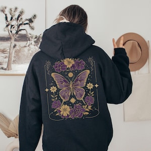 May include: Black hooded sweatshirt with a purple butterfly and floral design on the back. The butterfly has gold accents and is surrounded by flowers in shades of purple and gold.