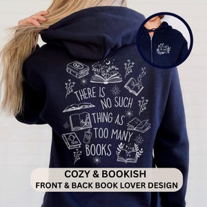 May include: Navy blue zip-up hoodie with a white graphic on the back featuring open books, stars, and the text "THERE IS NO SUCH THING AS TOO MANY BOOKS." A smaller graphic is on the front. The text "COZY & BOOKISH FRONT & BACK BOOK LOVER DESIGN" is at the bottom.