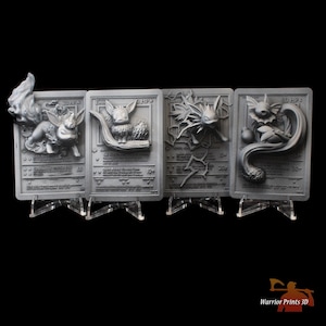 May include: Four 3D printed Pokemon cards featuring Eevee evolutions. The cards are grey and feature the Pokemon in a 3D sculpted design. The cards are on display stands.