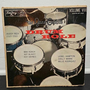 May include: Vintage vinyl record album cover for "Drum Roll" by The Jazz Greats. The cover features a collage of drum sets in various colors, with the album title in large red letters. Includes artist names.