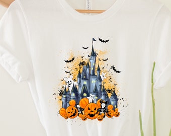 Puede incluir: Camiseta blanca con un gráfico de Halloween de un castillo, calabazas y fantasmas. El castillo es una silueta de un famoso castillo de parque temático.