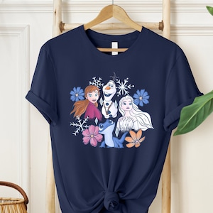 May include: A navy blue t-shirt with a graphic print of Anna, Elsa, Olaf, and Sven from the movie Frozen. The graphic is surrounded by snowflakes and flowers.