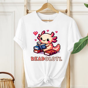 May include: White t-shirt with a pixelated illustration of an axolotl reading a book. The axolotl is pink and has a blue book. The text "READOLOTL" is printed below the axolotl.