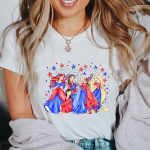 Op de afbeelding: Wit T-shirt met een afbeelding van Disney-prinsessen in rode, witte en blauwe jurken met vuurwerk op de achtergrond.