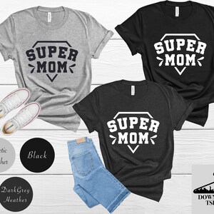 May include: Three t-shirts with the text "SUPER MOM" in a diamond shape. The shirts are in athletic heather, black, and dark grey heather.