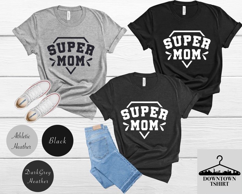 May include: Three t-shirts with the text "SUPER MOM" in a diamond shape. The shirts are in athletic heather, black, and dark grey heather.