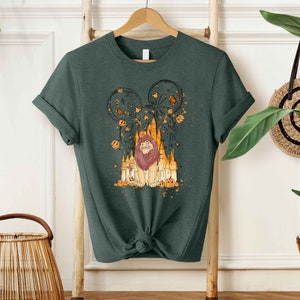 May include: A dark green t-shirt with a graphic print of a lion in front of a castle with fireworks and pumpkins. The lion is wearing a crown and has a golden mane.