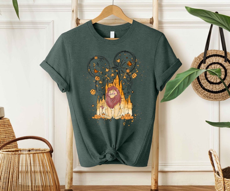 May include: A dark green t-shirt with a graphic print of a lion in front of a castle with fireworks and pumpkins. The lion is wearing a crown and has a golden mane.