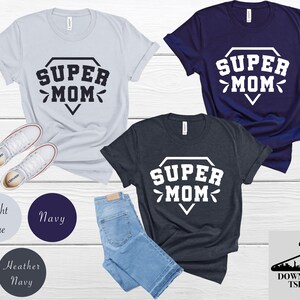 May include: Three t-shirts in different colors with the text "SUPER MOM" in a diamond shape. The t-shirts are available in light blue, navy blue, and heather navy.