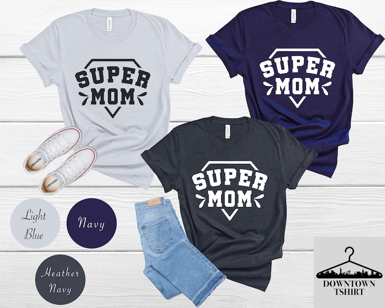 May include: Three t-shirts in different colors with the text "SUPER MOM" in a diamond shape. The t-shirts are available in light blue, navy blue, and heather navy.