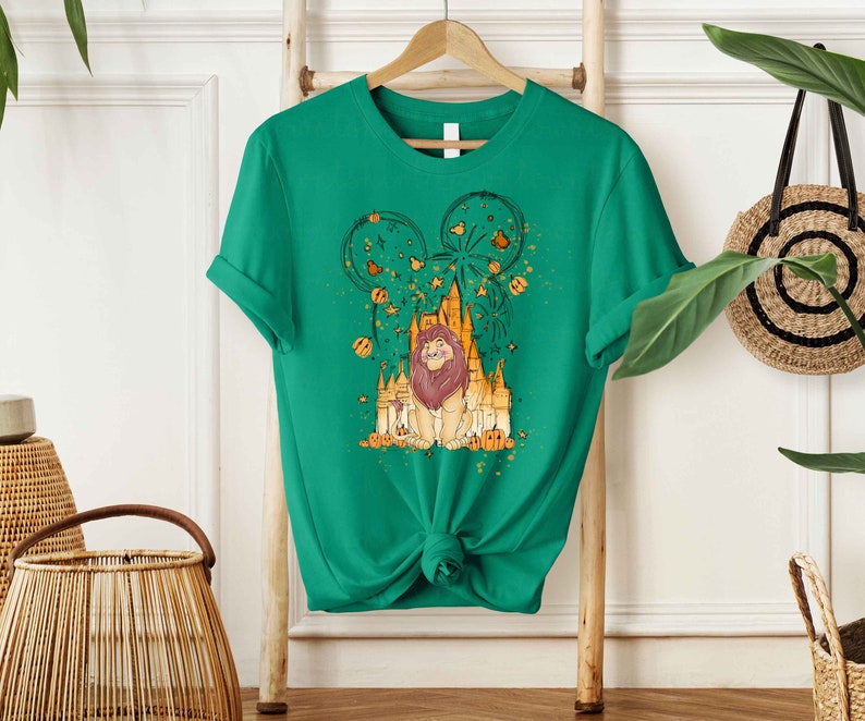 May include: Green t-shirt with a graphic print of a lion in front of a castle with fireworks and a Mickey Mouse ear silhouette. The graphic is in shades of yellow, orange, and brown.
