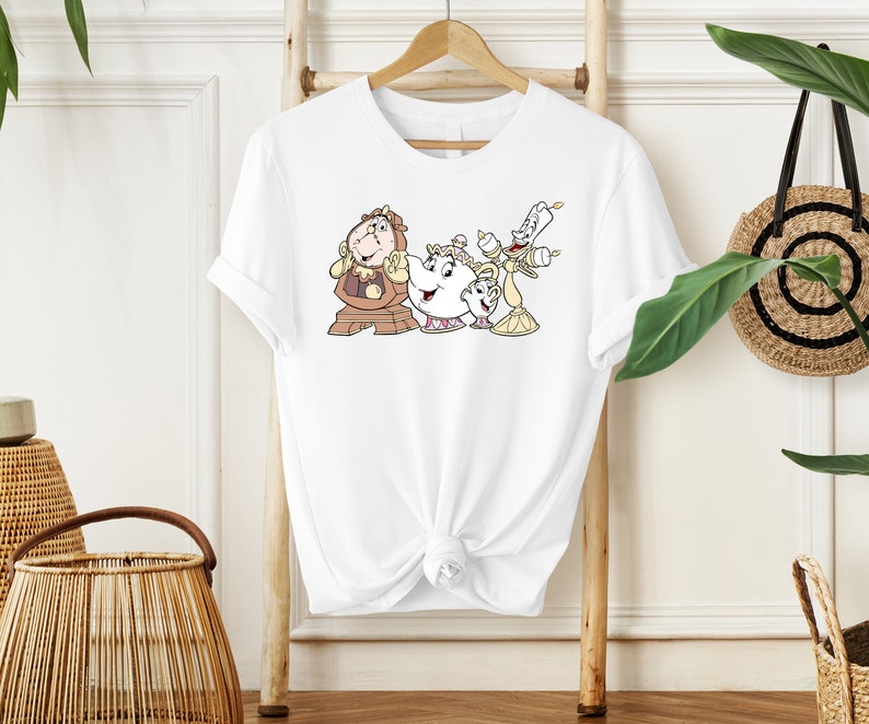 May include: White t-shirt with a graphic print of characters from the Disney movie Beauty and the Beast. The characters are Cogsworth, Mrs. Potts, and Lumiere.