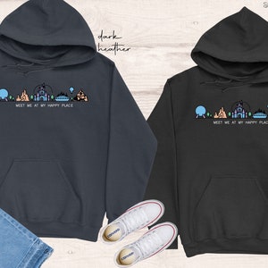 Op de afbeelding: Twee hoodies in donker grijs en zwart met een afbeelding van een Disney-themapark skyline en de tekst "Meet me at my happy place".