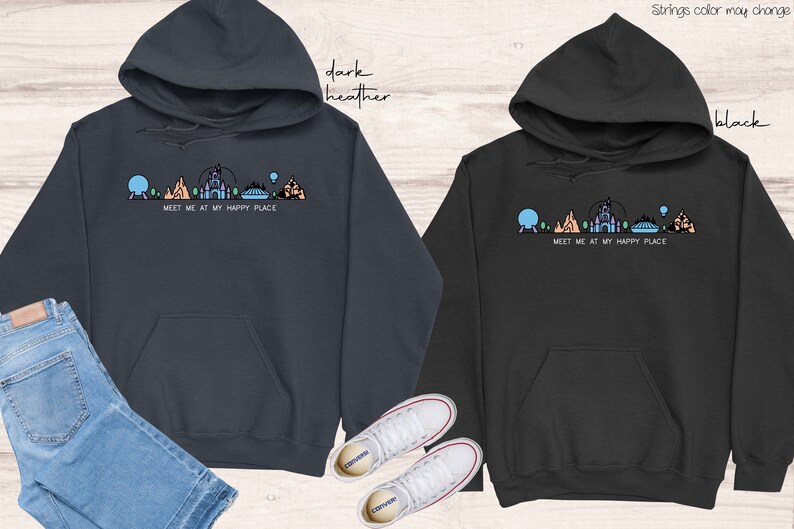 Op de afbeelding: Twee hoodies in donker grijs en zwart met een afbeelding van een Disney-themapark skyline en de tekst "Meet me at my happy place".