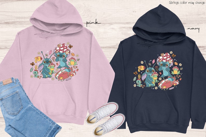 May include: Two hooded sweatshirts with a cartoon design of Stitch from Lilo & Stitch. The pink sweatshirt has a pink hood and the navy sweatshirt has a navy hood. Both sweatshirts feature a design of Stitch with mushrooms, flowers, and other nature-themed elements.