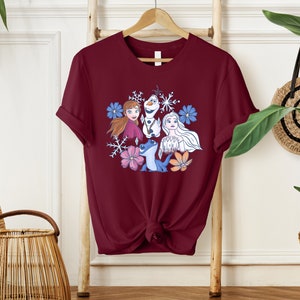 May include: A maroon t-shirt with a graphic print of characters from the movie Frozen. The characters are surrounded by snowflakes and flowers.