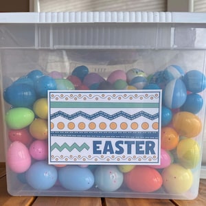 May include: A clear plastic container filled with colorful plastic Easter eggs. A label on the front of the container reads "Easter" with a decorative border.