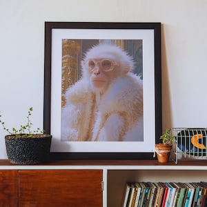 May include: Framed art print featuring a white monkey wearing clear glasses and a fluffy white coat. The monkey is set against a detailed, golden background. The print is displayed on a dark brown shelf with a plant and records.