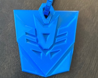 May include: A blue plastic keychain shaped like the Autobot symbol from the Transformers franchise. The keychain has a loop at the top for attaching to keys.