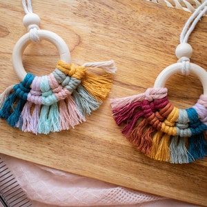 May include: Two wooden ring necklaces with colorful macrame tassels. The tassels are made with a variety of colors, including teal, pink, yellow, and orange.