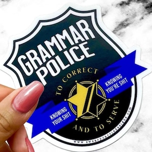 May include: A sticker with a police badge design. The badge is black and white with the words "GRAMMAR POLICE" in white. A blue ribbon across the badge reads "TO CORRECT" and "KNOWING YOU'RE SHIT". A gold star is in the center.