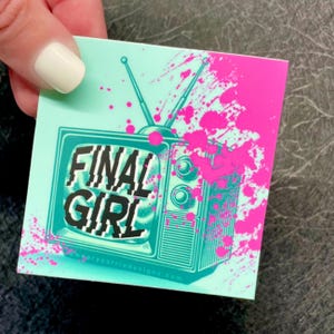 K&ouml;nnte beinhalten: Ein blaugr&uuml;ner Aufkleber mit einem Retro-Fernseher, auf dem der Text "FINAL GIRL" zu sehen ist. Auf dem Fernseher und dem Hintergrund befinden sich rosa Farbschleier.