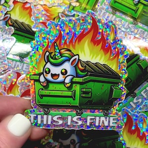 May include: A holographic sticker featuring a cartoon unicorn in a green dumpster on fire. The sticker has the text "This is fine." printed on it.