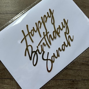 May include: Gold glitter cake topper with the text "Happy Birthday Sarah" in a cursive font.