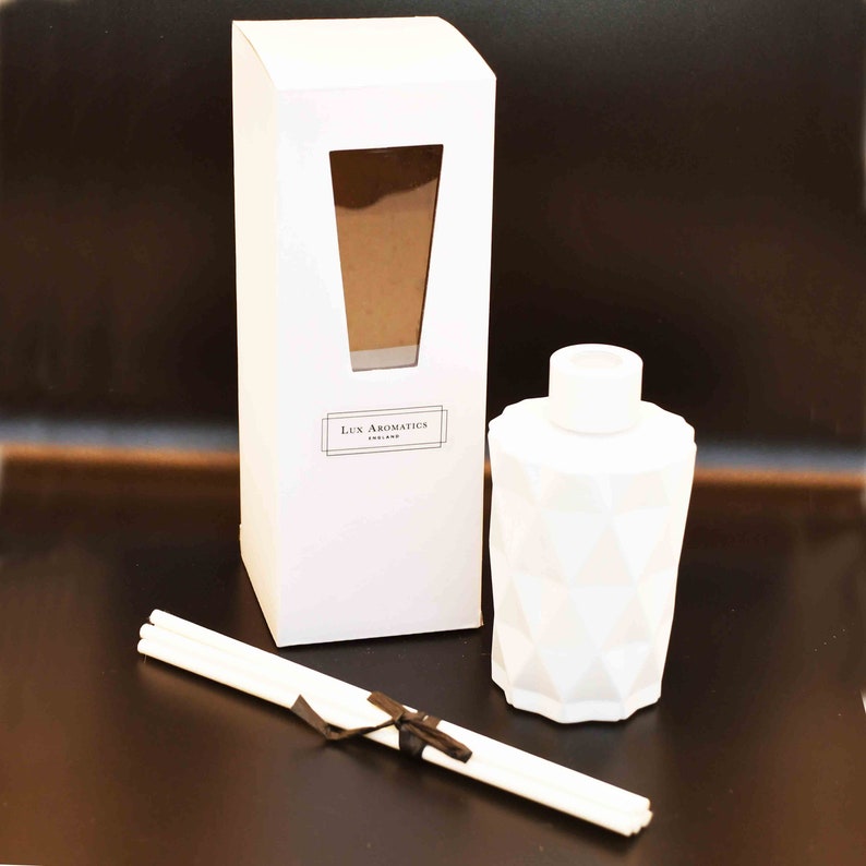 Puede incluir: Un difusor blanco con dise&ntilde;o geom&eacute;trico, una caja a juego y varillas. La caja tiene una ventana. El texto "Lux Aromatics ENGLAND" est&aacute; impreso en la caja. Las varillas est&aacute;n atadas con una cinta marr&oacute;n oscuro.