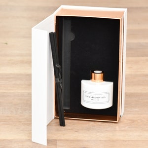 May include: A white aromatherapy diffuser set in a decorative box with rose gold trim. The set includes a white ceramic bottle with rose gold accents, black reeds, and the text "Lux Aromatics ENGLAND". The box is white with rose gold trim.