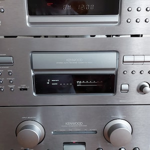 Pu&ograve; includere: Un sistema stereo Kenwood argentato con un lettore CD, un registratore a cassette e un amplificatore. Il sistema ha un display digitale e diversi pulsanti per controllare le funzioni.