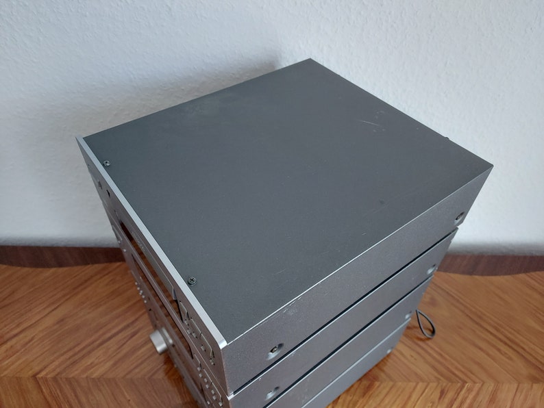 Pu&ograve; includere: Un sistema stereo impilabile color argento con tre componenti. Il componente superiore ha una superficie piatta e liscia.