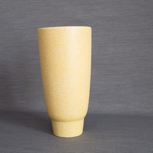 May include: A yellow ceramic vase with a speckled texture. The vase has a cylindrical shape with a slightly flared base.
