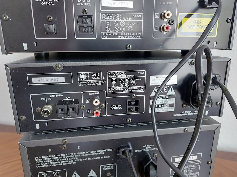 Pu&ograve; includere: Vista posteriore di un sistema stereo Kenwood nero con un lettore CD, un sintonizzatore e un amplificatore. Il sistema ha una piastra frontale argentata e un pannello di controllo nero. La parte posteriore del sistema ha vari jack di ingresso e uscita, tra cui antenna, altoparlanti e connessioni audio. Il sistema &egrave; etichettato "Kenwood Corporation" e "Made in Singapore".