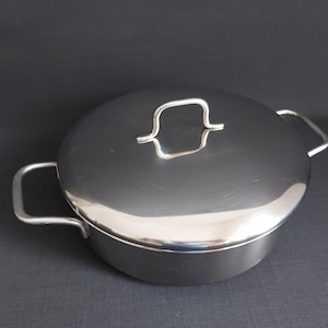 May include: A stainless steel pot with a lid and two handles. The pot has a shiny, reflective surface.