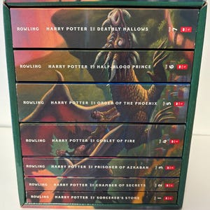 May include: A boxed set of seven Harry Potter books by J.K. Rowling, arranged vertically. The spines feature colourful fantasy illustrations of creatures and characters, with white text indicating the title, author, and year for each volume.