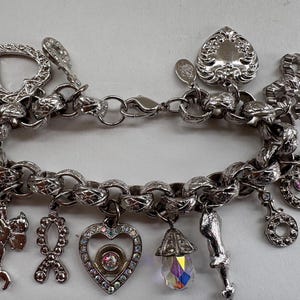 May include: Silver charm bracelet with various charms, including a heart, bow, and cherub. The bracelet features a chunky chain and a mix of textures and embellishments. Some charms have colorful accents.